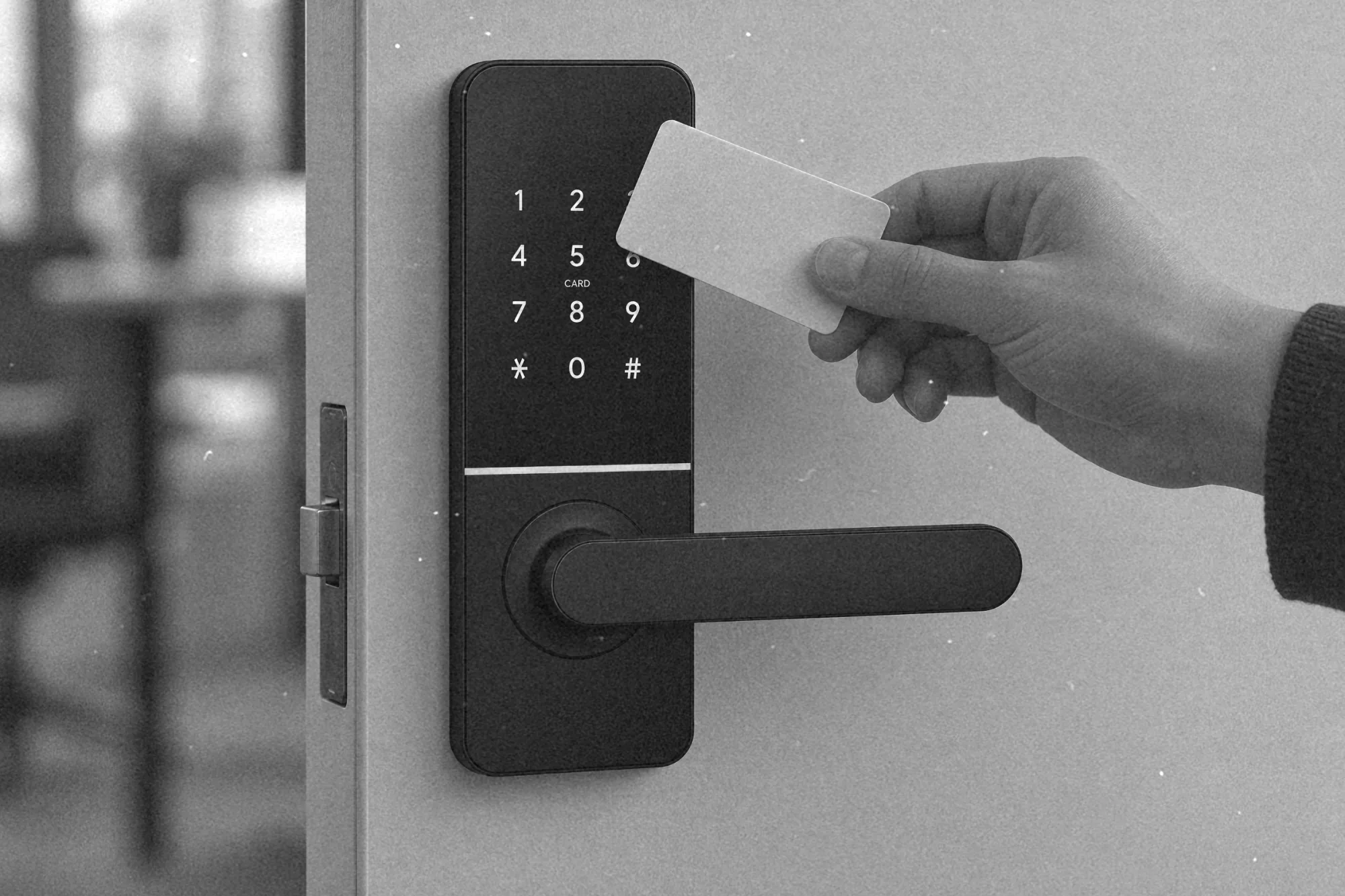 Dłoń przykłada kartę do elektronicznej klamki, obok drzwi z mechanicznymi wkładkami