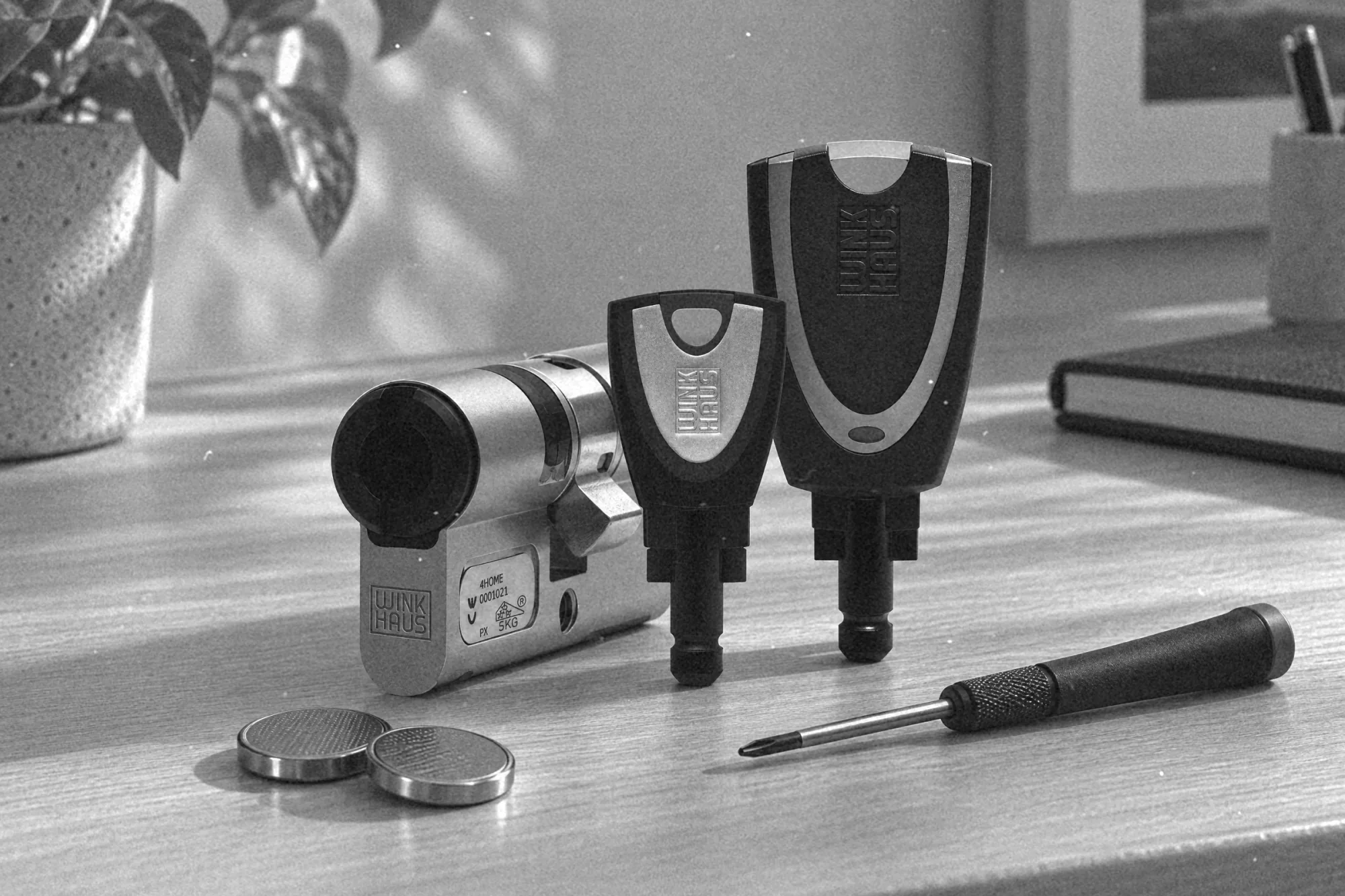 Dłoń wymienia baterię w otwartej klamce elektronicznej, na biurku narzędzia