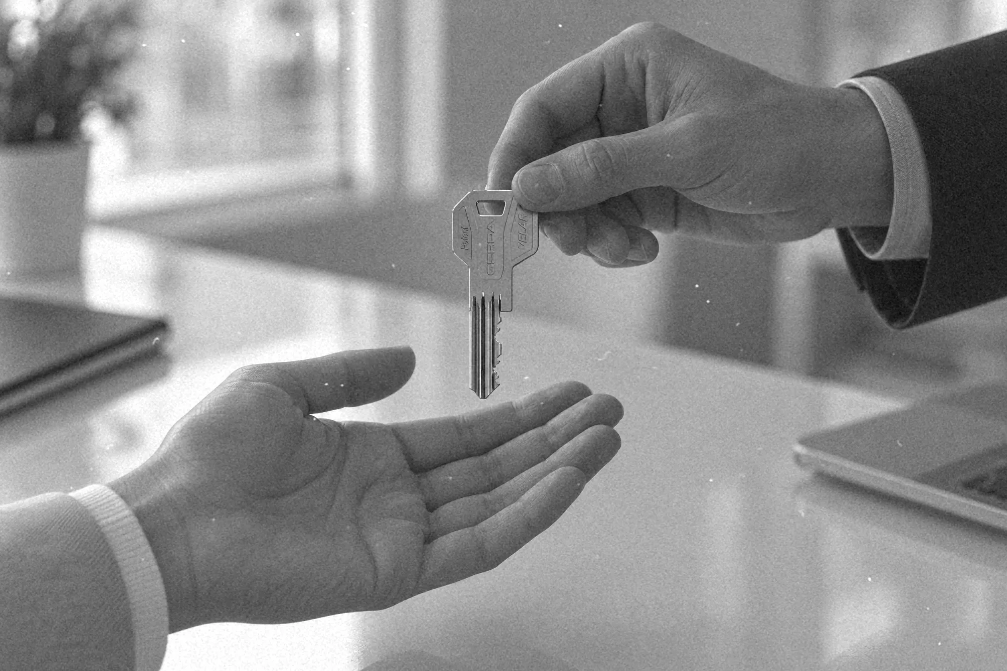 Dłoń przekazuje drugiej dłoni klucz dormakaba nad stołem w biurze zarządcy